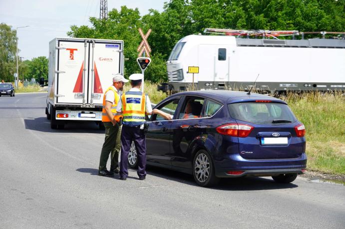 Ellenőrzés egy vasúti átjárónál, miközben a háttérben vonat halad el.